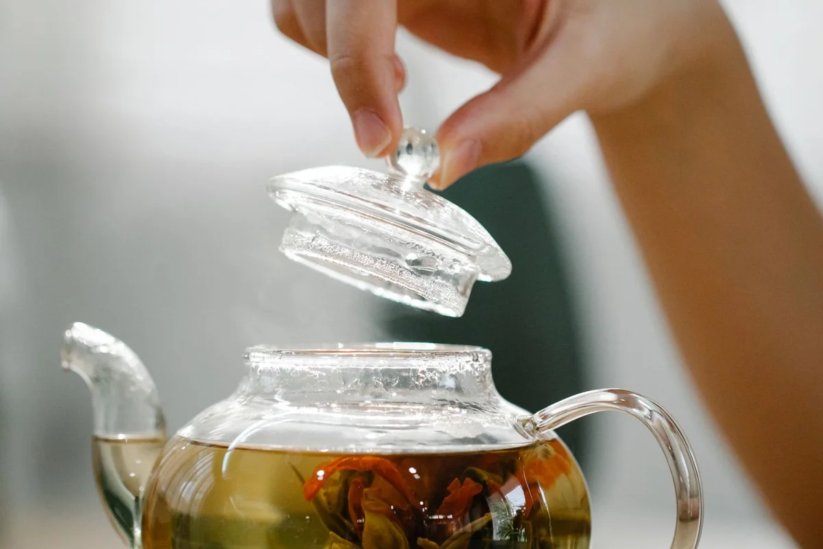 A hand placing the lid on a glass teapot