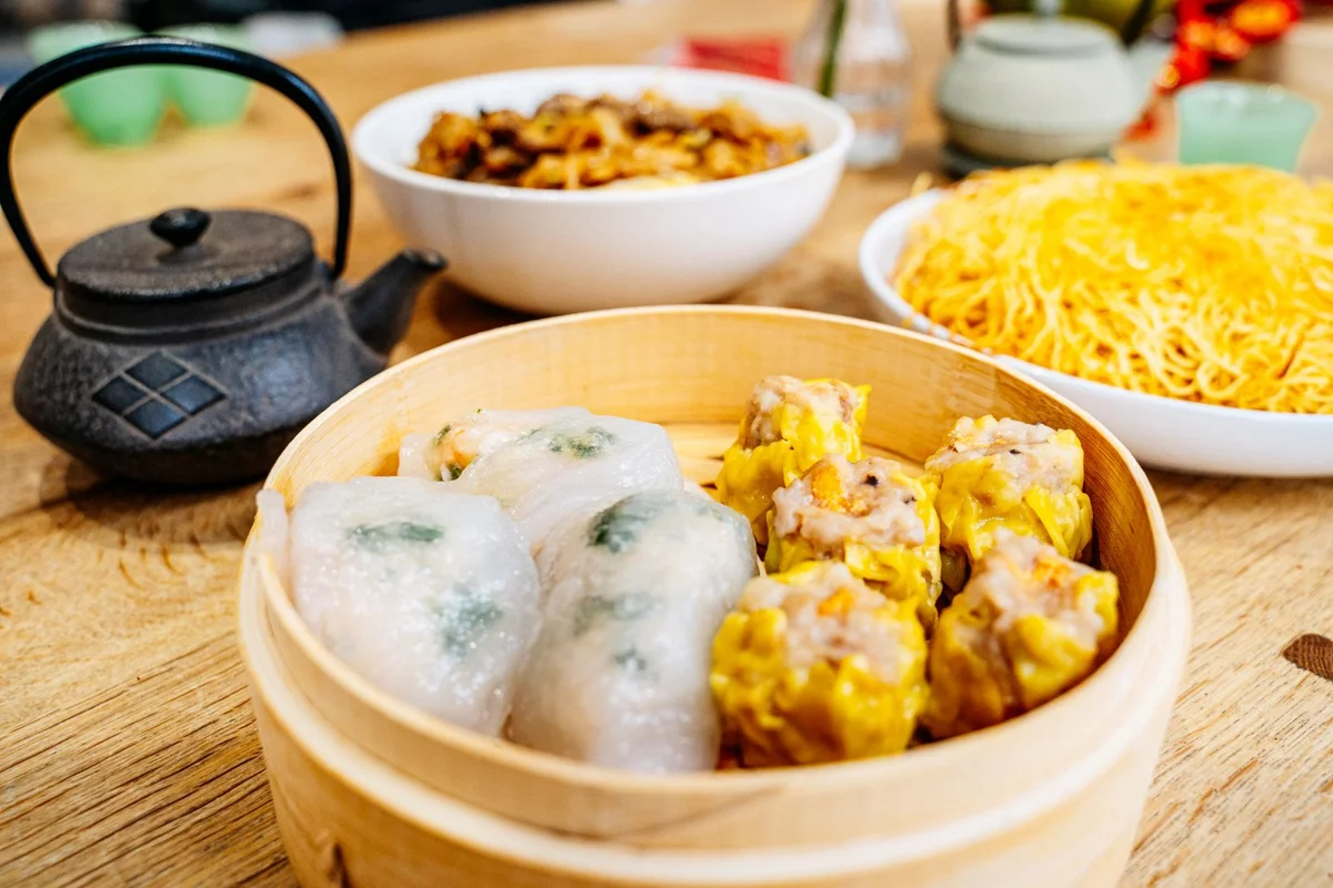 A dark teapot beside dim sum in a bamboo steamer