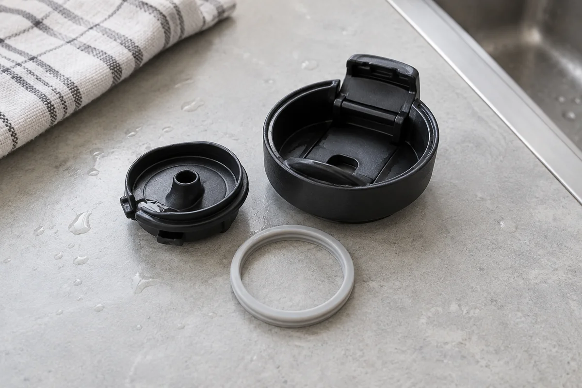 A travel mug lid and its removable silicone seal separated for cleaning