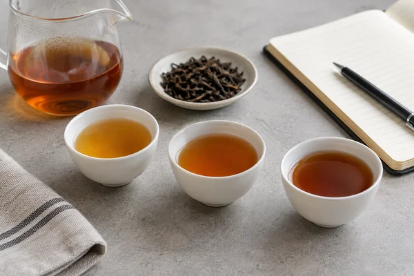 Three small white tea cups with subtly different amber liquor beside a notebook