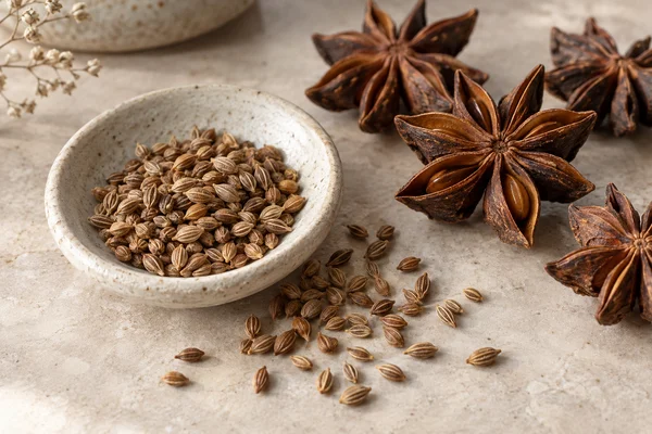 Small anise fruits and star-shaped star anise arranged in separate dishes