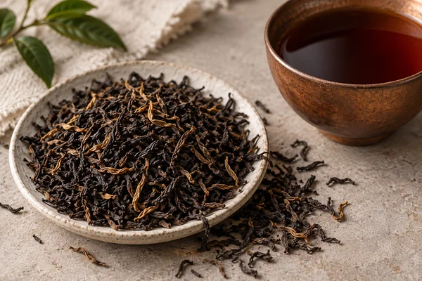 Dark Assam leaves with golden tips beside copper-brown tea