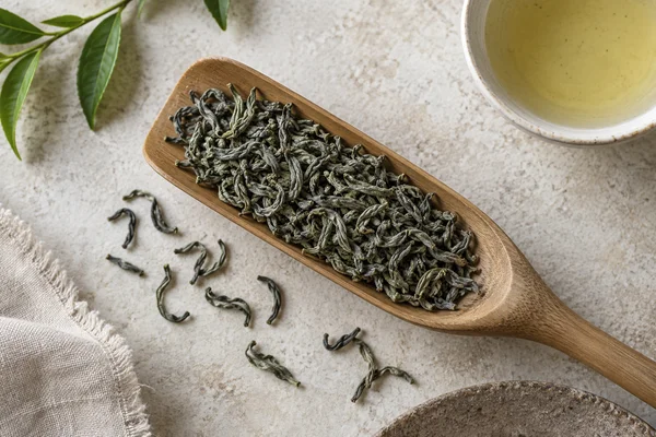 Slender curved grey-green Chun Mee leaves on a tea scoop