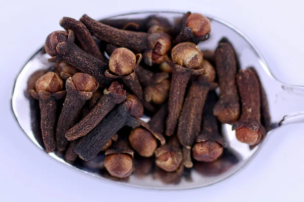 Whole dried cloves piled on a metal teaspoon