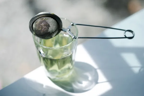 A tea infuser lifted above a glass of tea