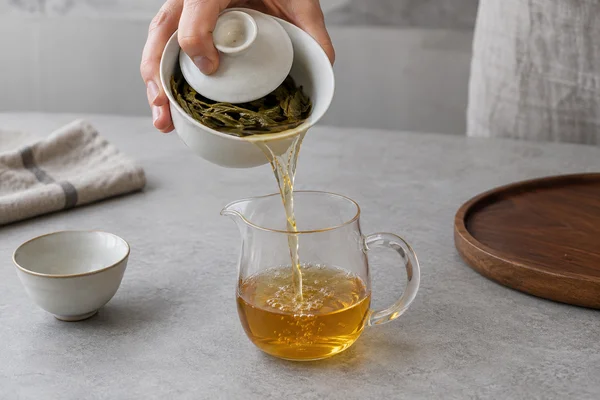 Tilted gaiwan draining into a small serving pitcher with wet leaves visible