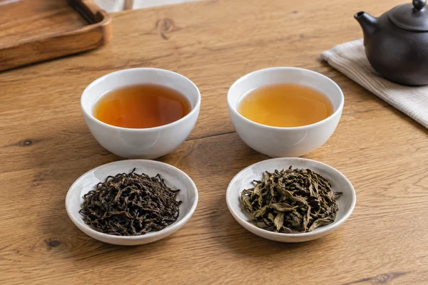 Two plain tasting bowls of amber tea with different dry leaf portions