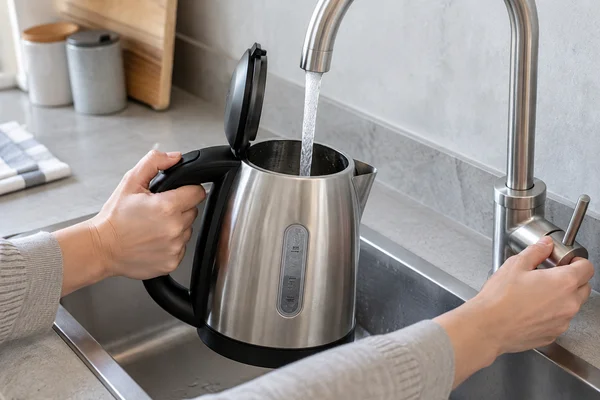 Clear water being added to an electric kettle at a kitchen sink