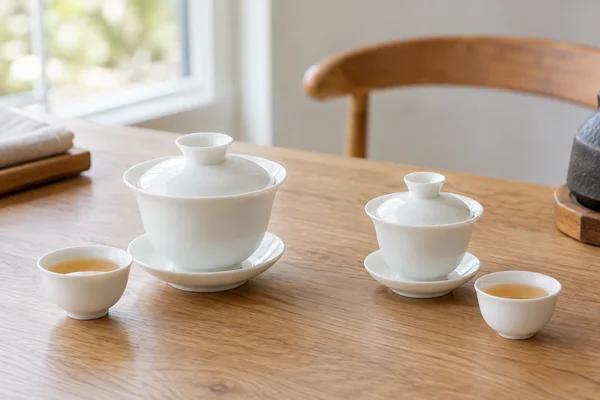 Two different sized white gaiwans side by side with small cups