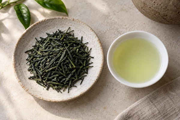 Dark gyokuro needles beside a tiny cup of pale jade tea