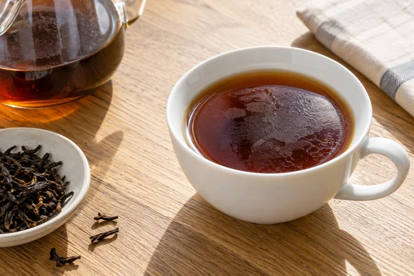 Fine surface film visible on black tea in a white cup under angled light