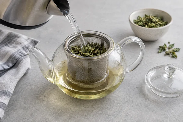 Water poured from a kettle onto dried herbs in a tea infuser