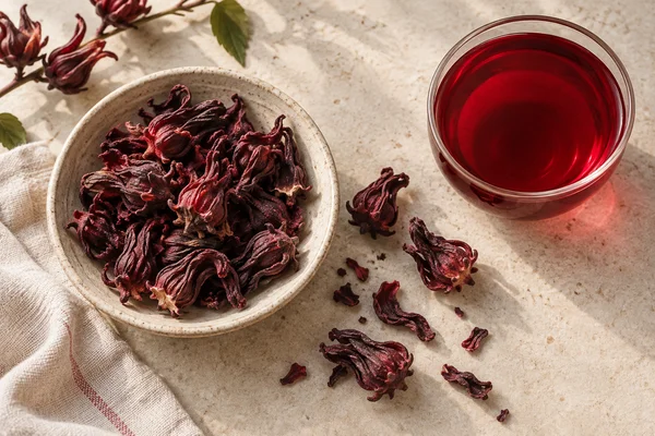 Deep red dried roselle calyces beside a ruby-coloured infusion