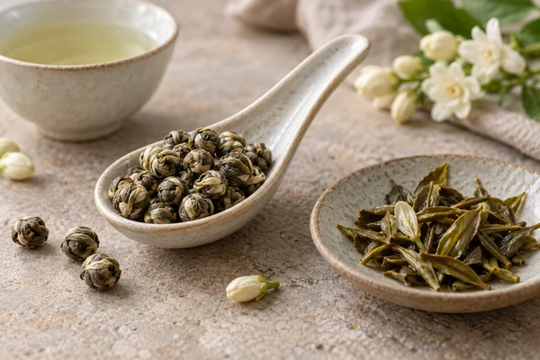 Pale green jasmine pearls on a spoon beside opened tea leaves
