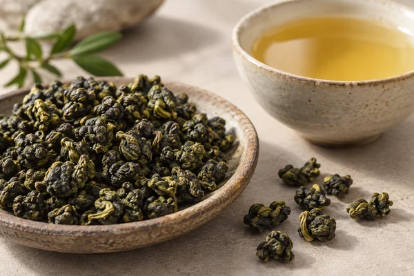 Plain rolled Jin Xuan leaves beside a clear golden infusion without milk