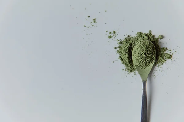 Fine green matcha powder on a spoon against a pale background