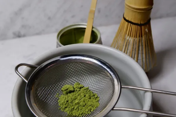 Matcha powder in a fine metal sieve above a bowl