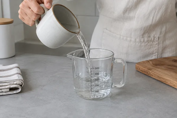 Water being measured from a ceramic mug into a clear graduated jug