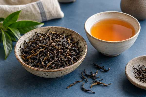 Wiry Nilgiri black tea leaves beside orange-gold tea