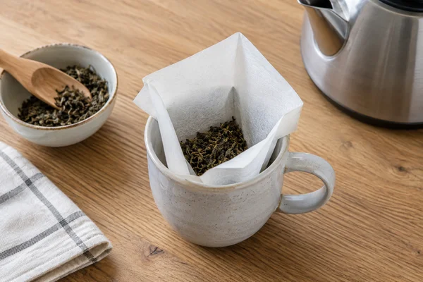 Open paper tea filter containing a modest amount of loose leaves in a mug