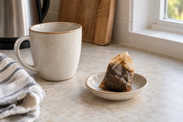 Used tea bag resting on a small ceramic dish beside a finished mug