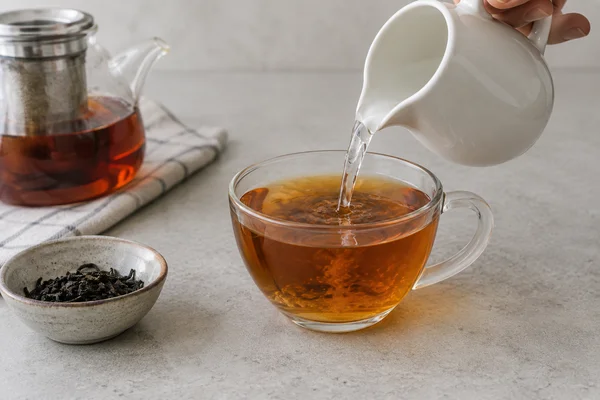 Small water pitcher adding water into a strong amber cup of tea