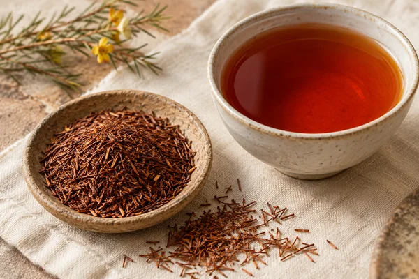 Fine red-brown rooibos pieces beside a reddish amber infusion
