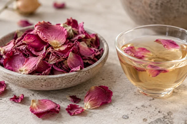 Food-grade dried pink rose petals beside a light floral infusion