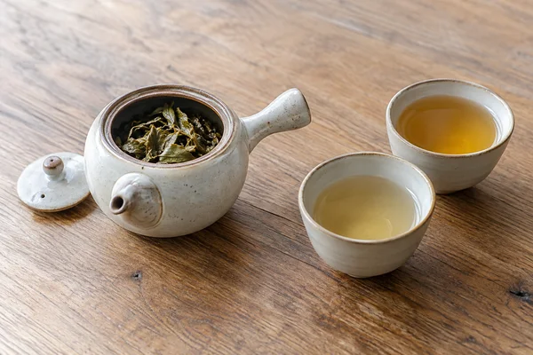 Opened tea leaves in a small pot beside two cups of different-coloured tea