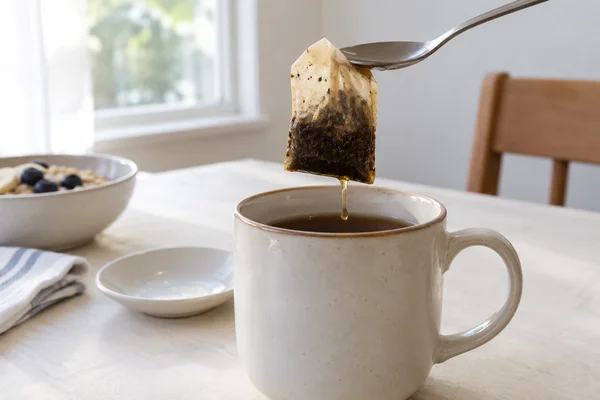 Wet tea bag held above a mug by a clean spoon without fingers near hot liquid