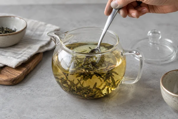 Spoon gently moving loose leaves in a glass brewing vessel