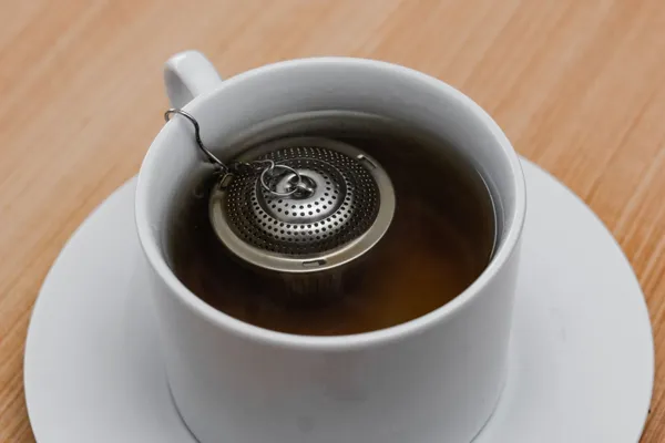 A small metal tea infuser in a white mug