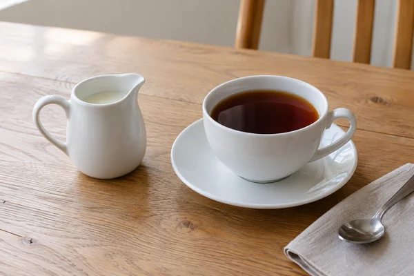 Small milk jug beside a completed cup of strong black tea