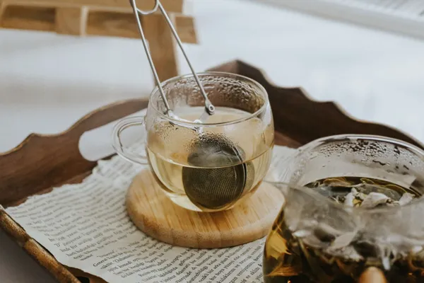 Glass teacups and a tea infuser on a wooden serving tray