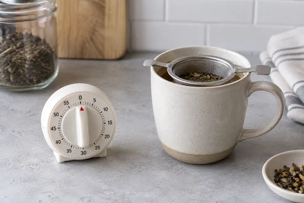 A standalone kitchen timer next to a cup with a tea infuser