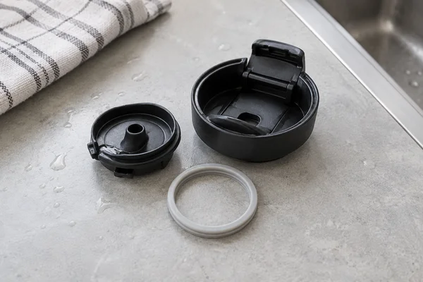 A travel mug lid and its removable silicone seal separated for cleaning