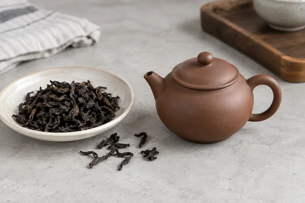 Small unglazed clay teapot beside roasted dark tea leaves