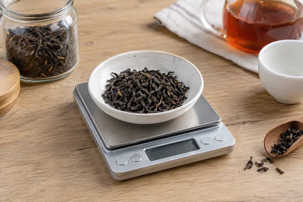 Loose black tea in a shallow weighing dish on a small digital scale