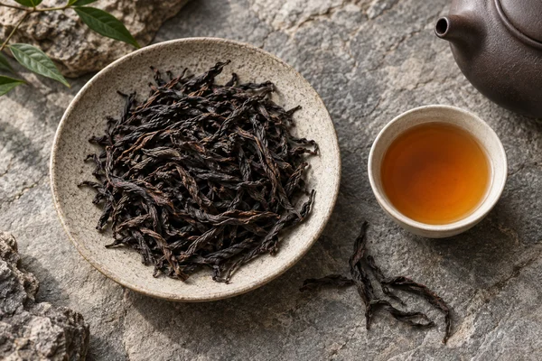Long dark Wuyi oolong leaves beside amber tea on grey stone