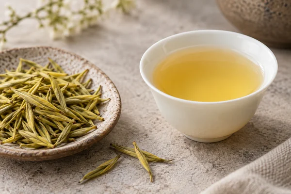 Slender yellow-green tea buds beside pale golden tea